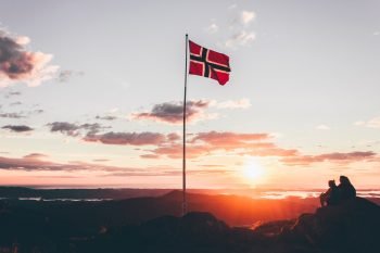 People sitting next to a Norway flag as the sun sets.